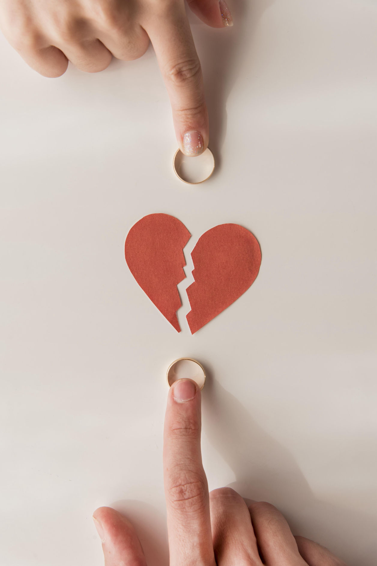 Dos manos señalando alianzas de boda sobre una mesa, con un corazón roto en el centro, simbolizando un divorcio o separación.